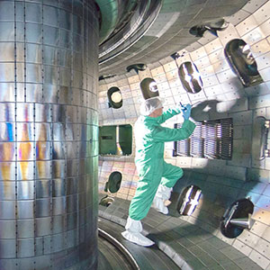 A person in a green jumpsuit uses a tool inside a vacuum vessel