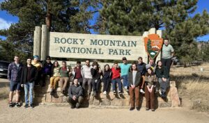 A group of people in front of a sign that reads "Rocky Mountain National Park"