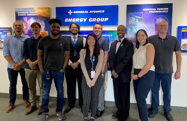 Nine graduate students stand in front of a sign reading "General Atomics - Energy Group"