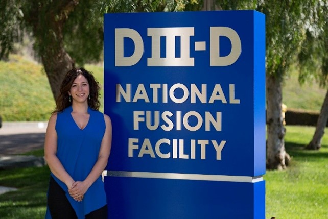 A scientist stands in front of a blue sign reading "DIII-D National Fusion Facility"