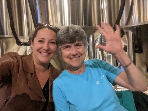 Two scientists sit in front of fermenter tanks at a brewery.