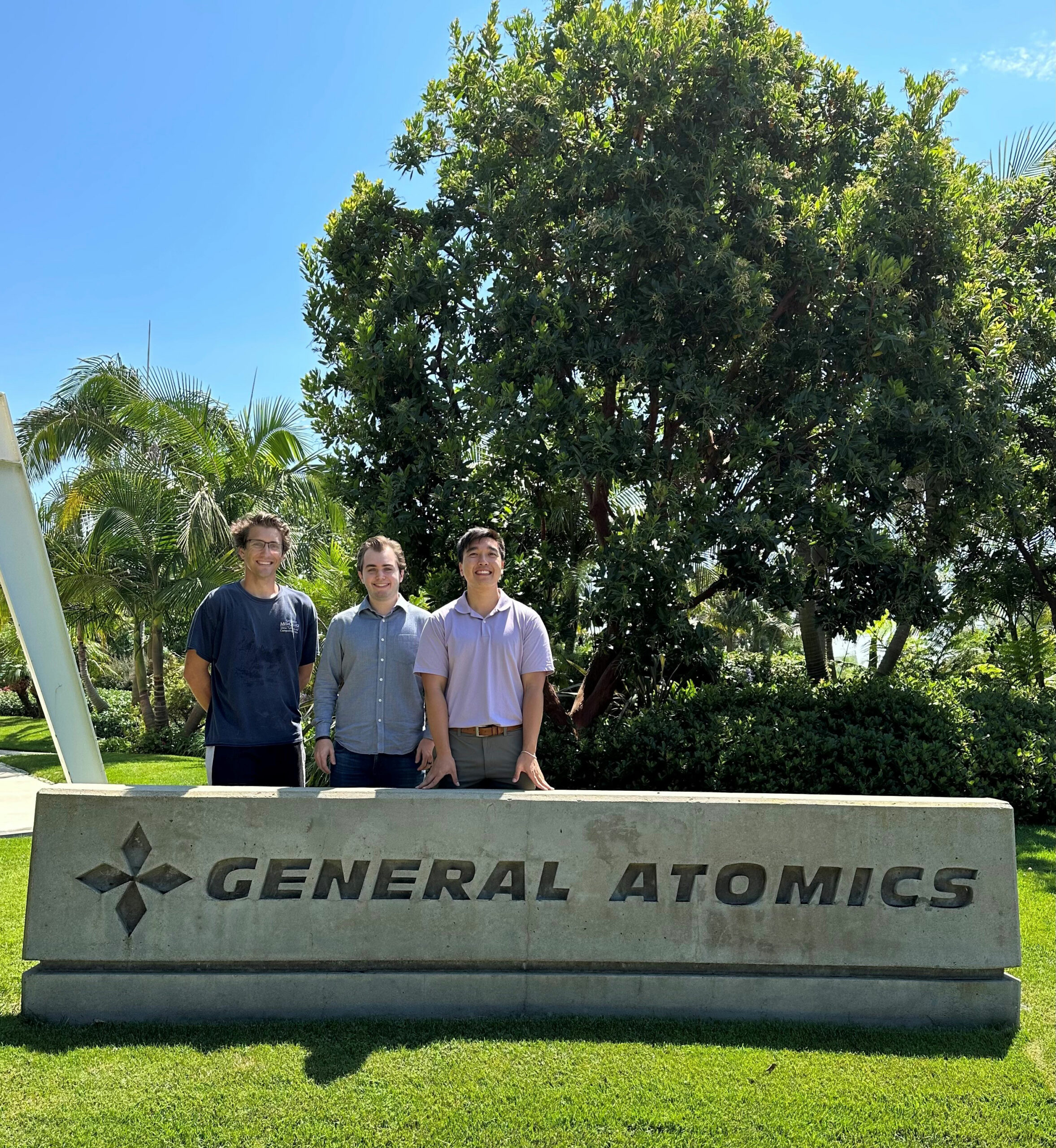 Three students stand behind a sign that reads "General Atomics"